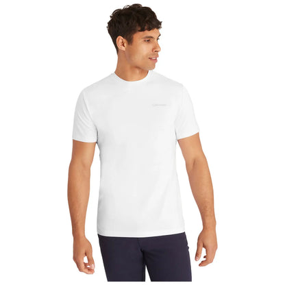 A young man stands confidently wearing a fitted white t-shirt with a small brand logo on the chest and dark pants against a plain white background.