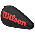 A black tennis racquet bag with a triangular shape displays a prominent red "Wilson" logo on its surface it is designed for carrying and protecting a tennis racquet