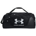 A black duffel bag displays a large silver Under Armour logo and carries a shoulder strap alongside two handles in a plain background.