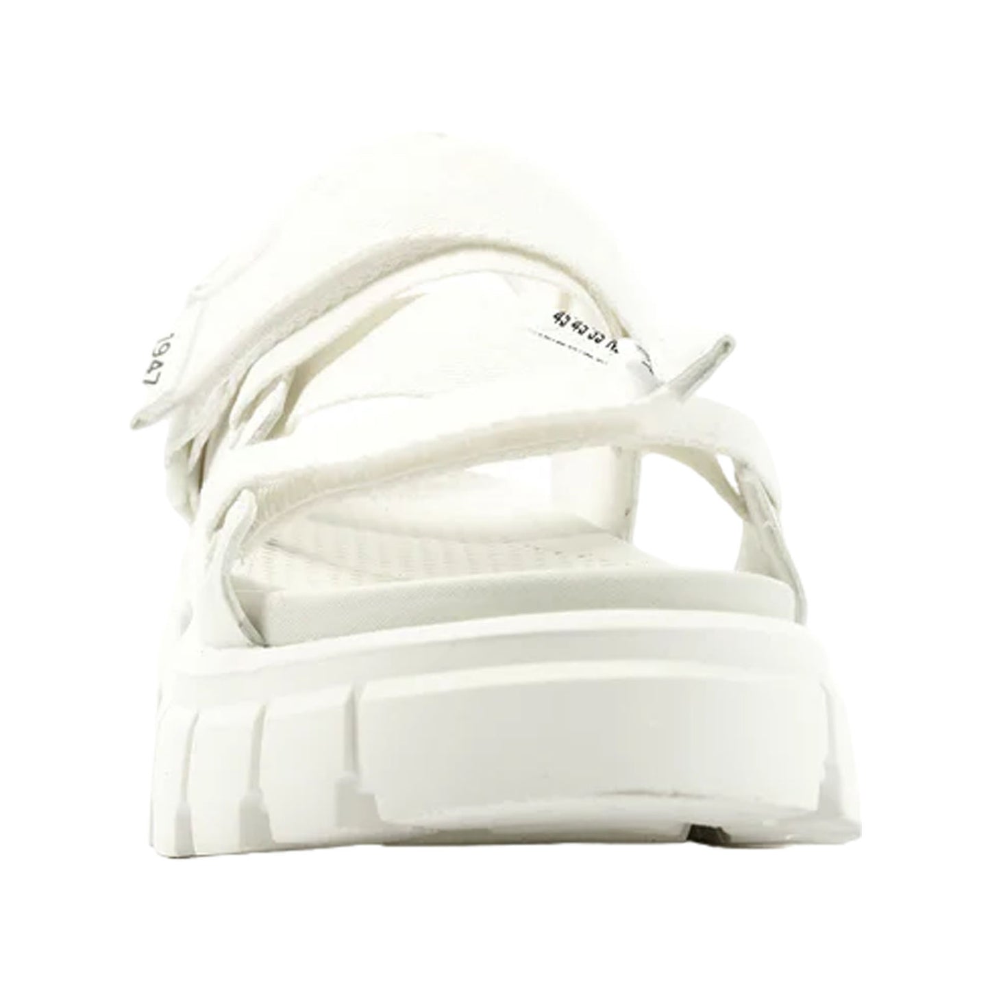 A white sandal with multiple adjustable straps is positioned upright showcasing a thick sole and textured footbed in a minimalist context against a neutral background