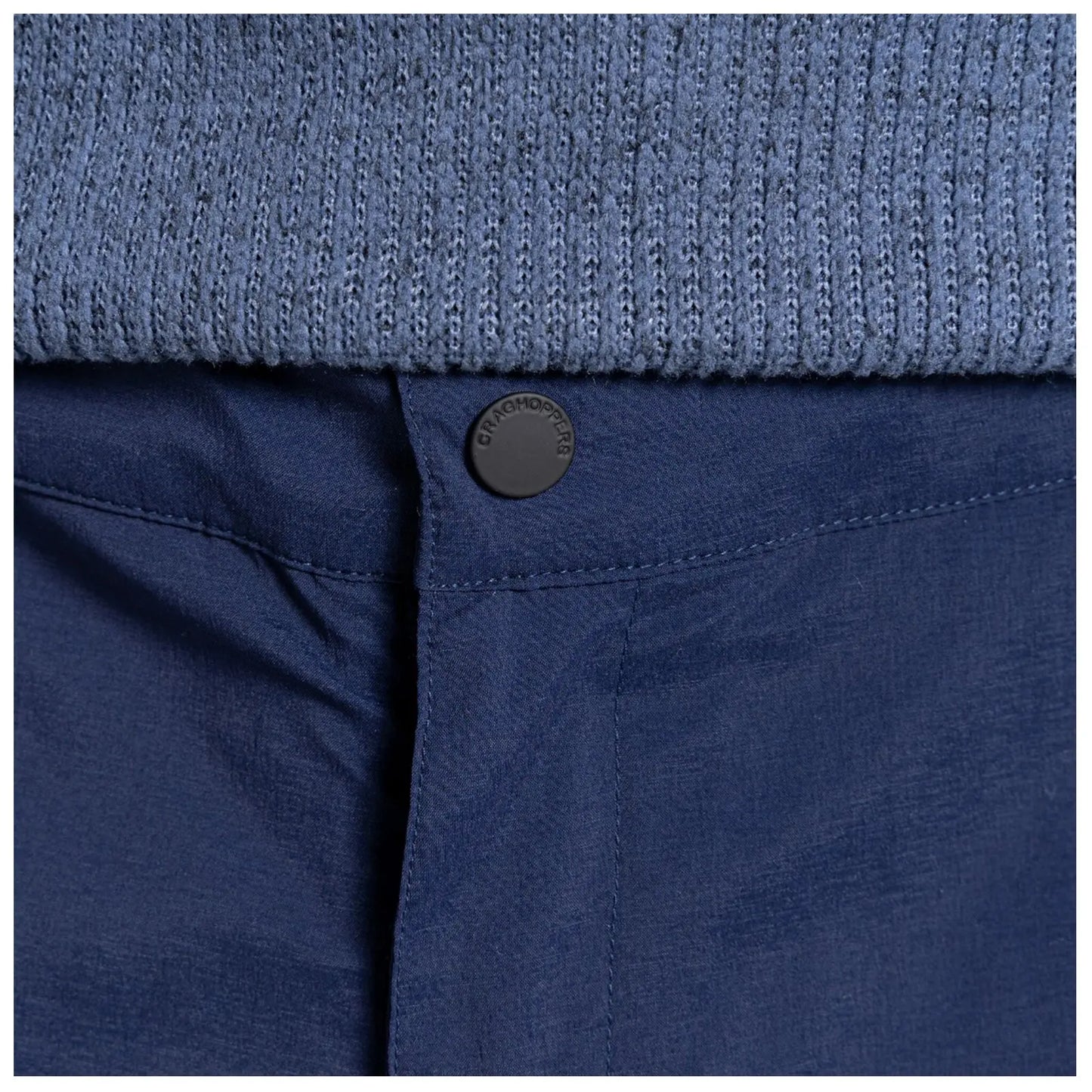 A navy blue fabric waistband features a black button marked Craghoppers while underneath is a textured light blue knitted garment, suggesting a layered clothing style in a casual setting.