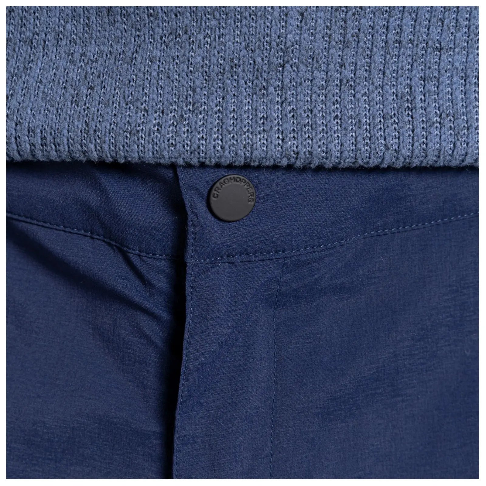 A navy blue fabric waistband features a black button marked Craghoppers while underneath is a textured light blue knitted garment, suggesting a layered clothing style in a casual setting.