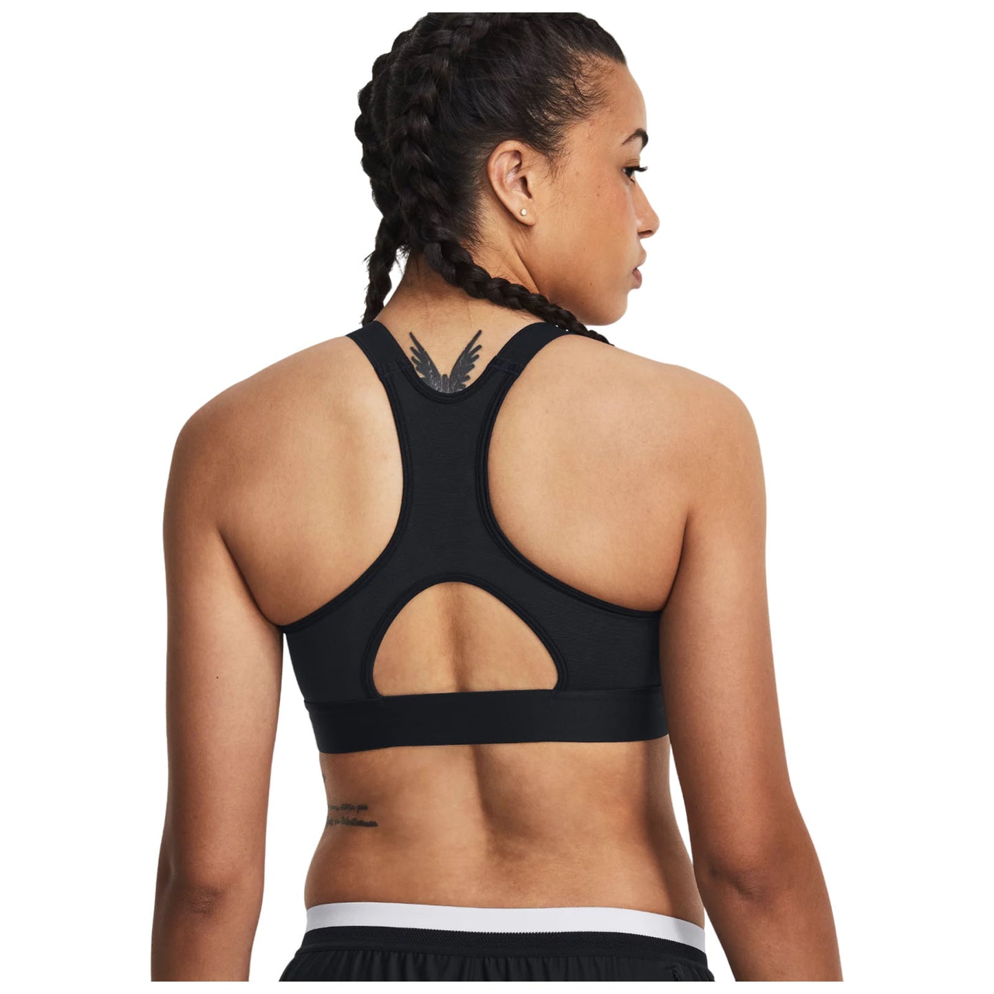 A woman with braided hair is wearing a black sports bra featuring a racerback design and a cutout detail on the back showcasing a tattoo on her shoulder.