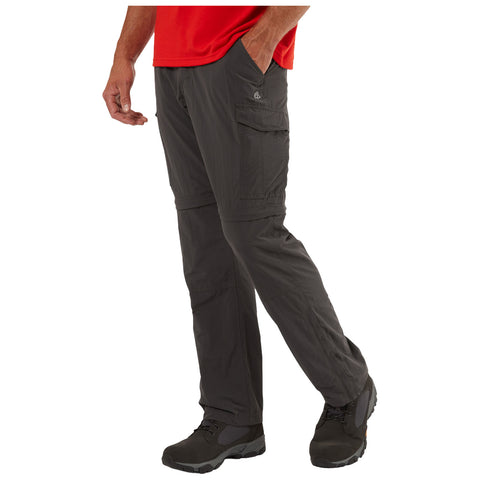 A person stands with one hand in their pocket wearing dark cargo pants and boots. They are dressed in a red shirt and appear to be ready for outdoor activities.
