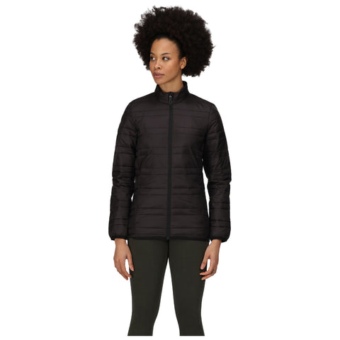 A woman with an afro stands upright wearing a black quilted jacket and green leggings while looking slightly to her right against a plain white background.