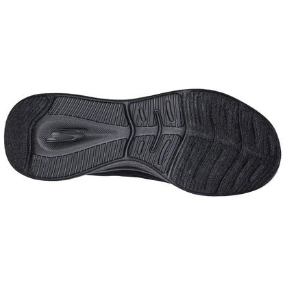 A shoe sole displays a textured black rubber surface designed for traction and comfort with a small logo visible in the center among various grooves and patterns.