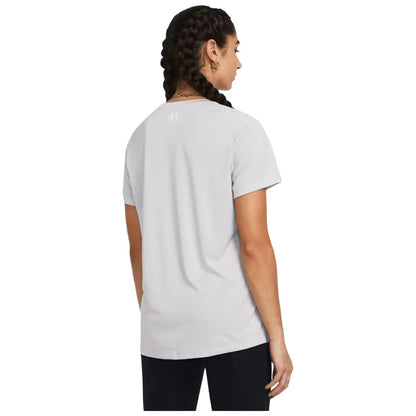 A person with braided hair is standing and facing away wearing a light gray t-shirt and black pants in a neutral background. The t-shirt has a subtle logo on the back.