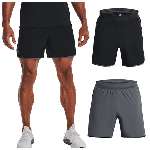 A person stands wearing black athletic shorts and white sneakers three pairs of shorts are displayed nearby in black and gray colors showcasing their design and style.