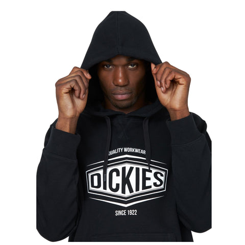 A person wears a black hoodie while pulling the hood over their head with a serious expression in a plain background without distractions. The hoodie displays the text "QUALITY WORKWEAR DICKIES SINCE 1922."