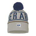 A gray knit beanie with a blue pom-pom on top features the word UNDER ARM in large blue letters and a white Under Armour logo at the bottom.