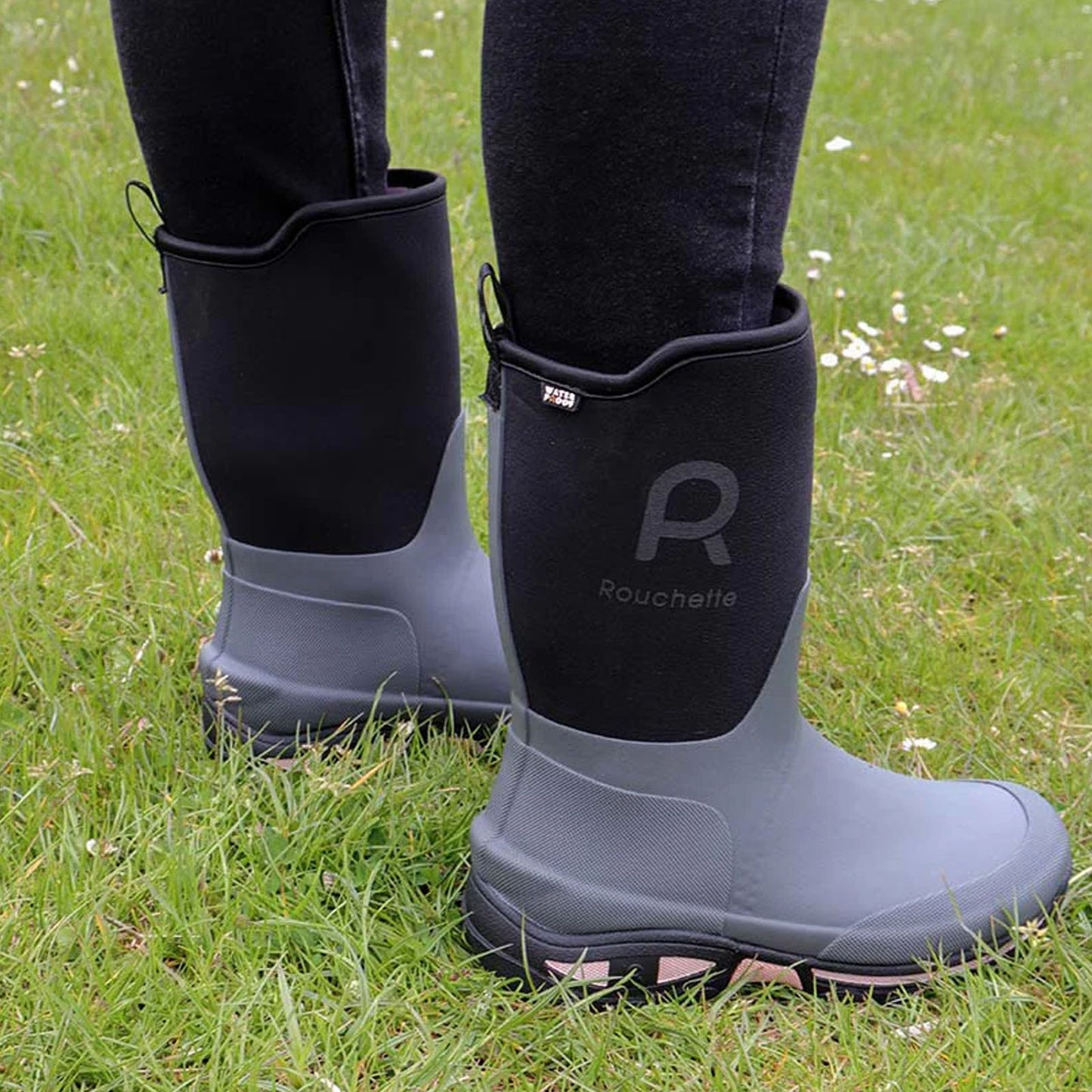 Rubber boots stand on green grass with a fabric upper and a logo "Rouchette" visible on the side while the wearer appears ready for outdoor activities.
