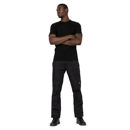 A man stands confidently with arms crossed wearing a black T-shirt and dark pants in a plain white background suggesting a casual or promotional context.