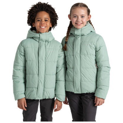 Two children stand side by side wearing light green puffy jackets with hoods smiling at the camera in a plain white background highlighting their joyful demeanor and casual attire.