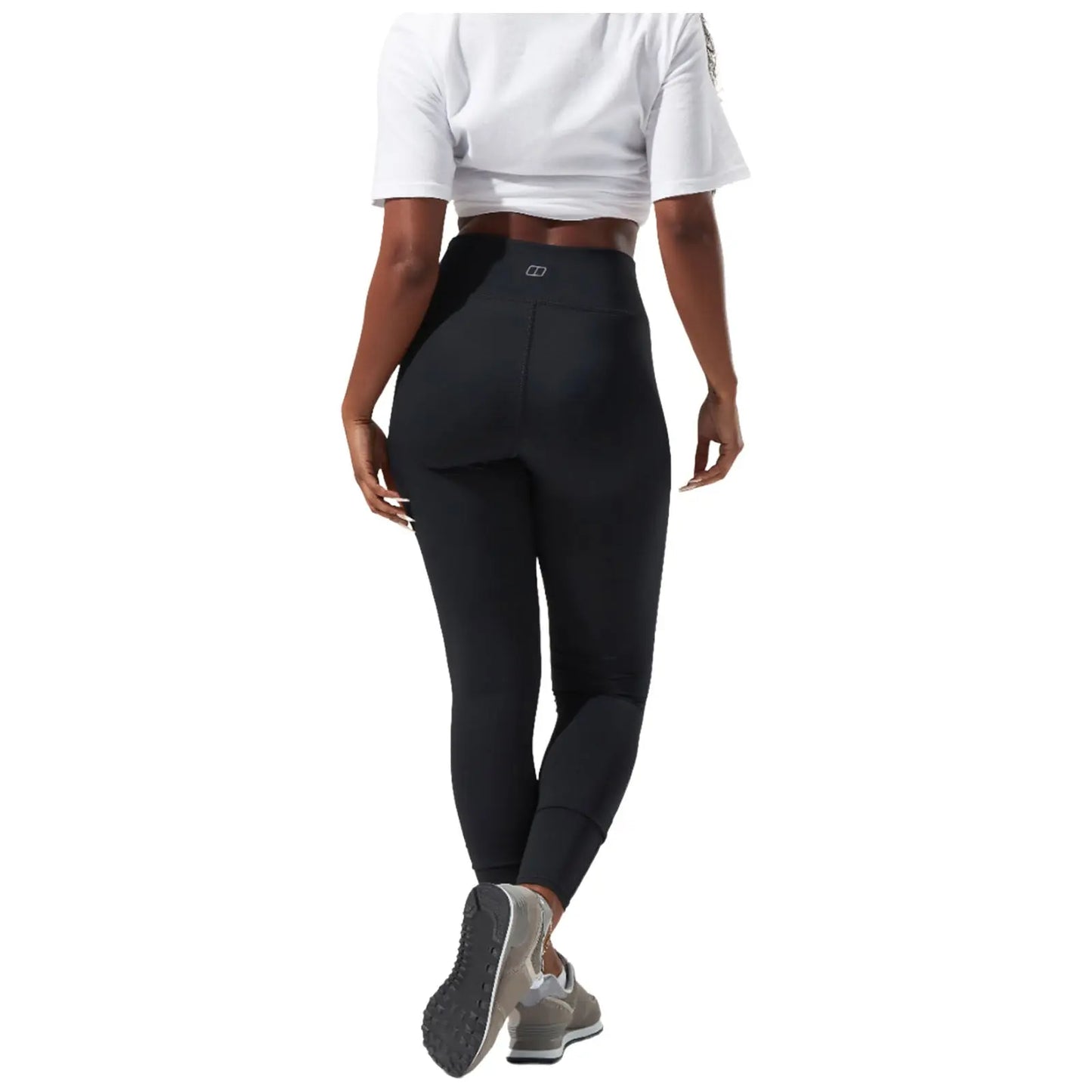 A person wearing olive green leggings and a white shirt is stretching, showcasing the form-fitting clothing. The background is plain and bright, emphasizing the outfit.