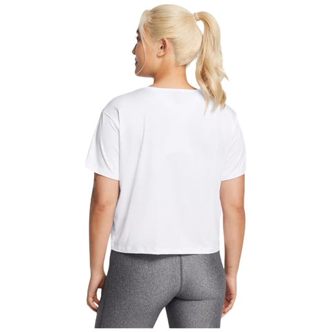 A person with light blonde hair tied in a ponytail wears a short white shirt and gray leggings while standing with their back turned in a plain background.