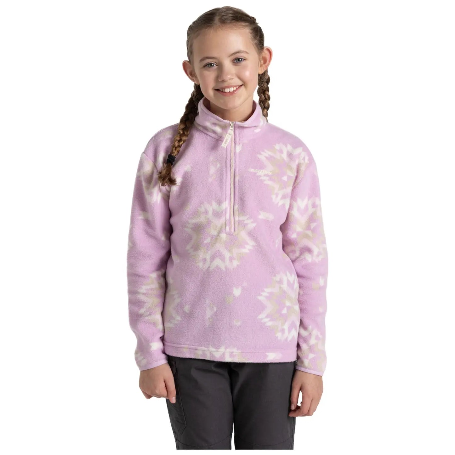 A young girl stands smiling in a cozy pink fleece pullover with a zippered neck. She has two braids and is wearing dark pants, against a plain white background.