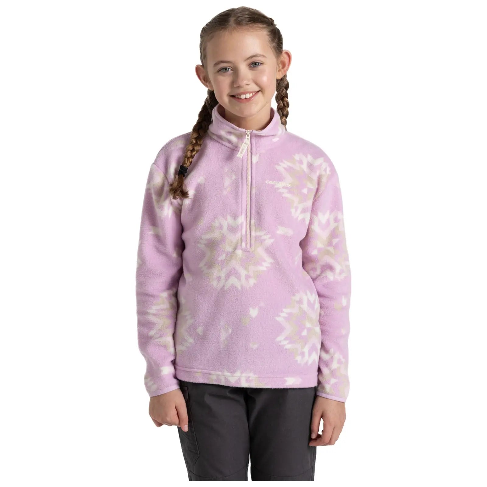 A young girl stands smiling in a cozy pink fleece pullover with a zippered neck. She has two braids and is wearing dark pants, against a plain white background.