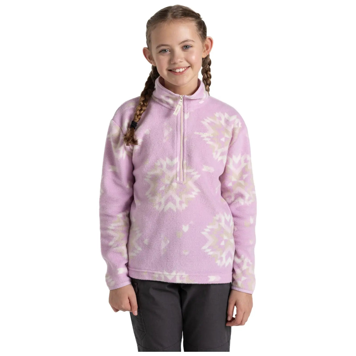 A young girl stands smiling in a cozy pink fleece pullover with a zippered neck. She has two braids and is wearing dark pants, against a plain white background.
