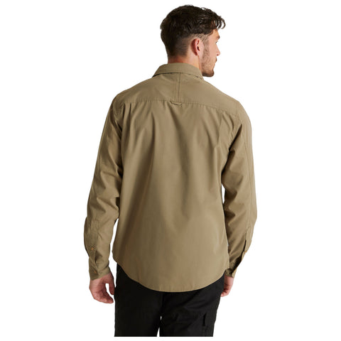 A person stands with their back facing the viewer wearing a light brown long-sleeved shirt and black pants in a well-lit, neutral background environment.