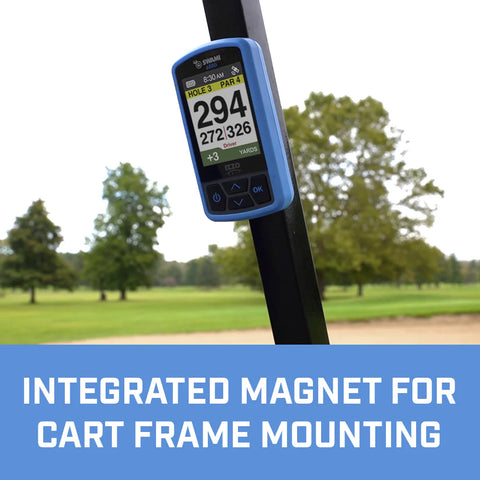 A golf GPS device is mounted on a cart frame displaying hole information and distance measurements in a green golf course environment with trees in the background. Integrated magnet for cart frame mounting.