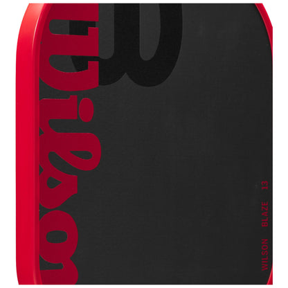 A red paddle with a black hitting surface displays the word "Wilson" prominently in red and black. The paddle is designed for racquet sports, likely in a sporting goods context.