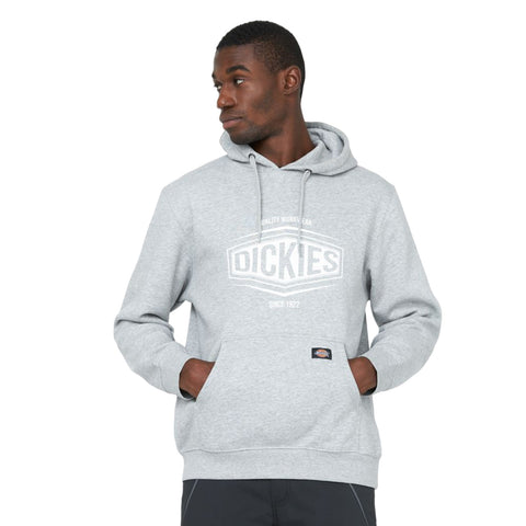 A man wearing a gray hoodie with the brand name Dickies displayed prominently stands with his hands in the pockets gazing slightly to the side against a plain background.