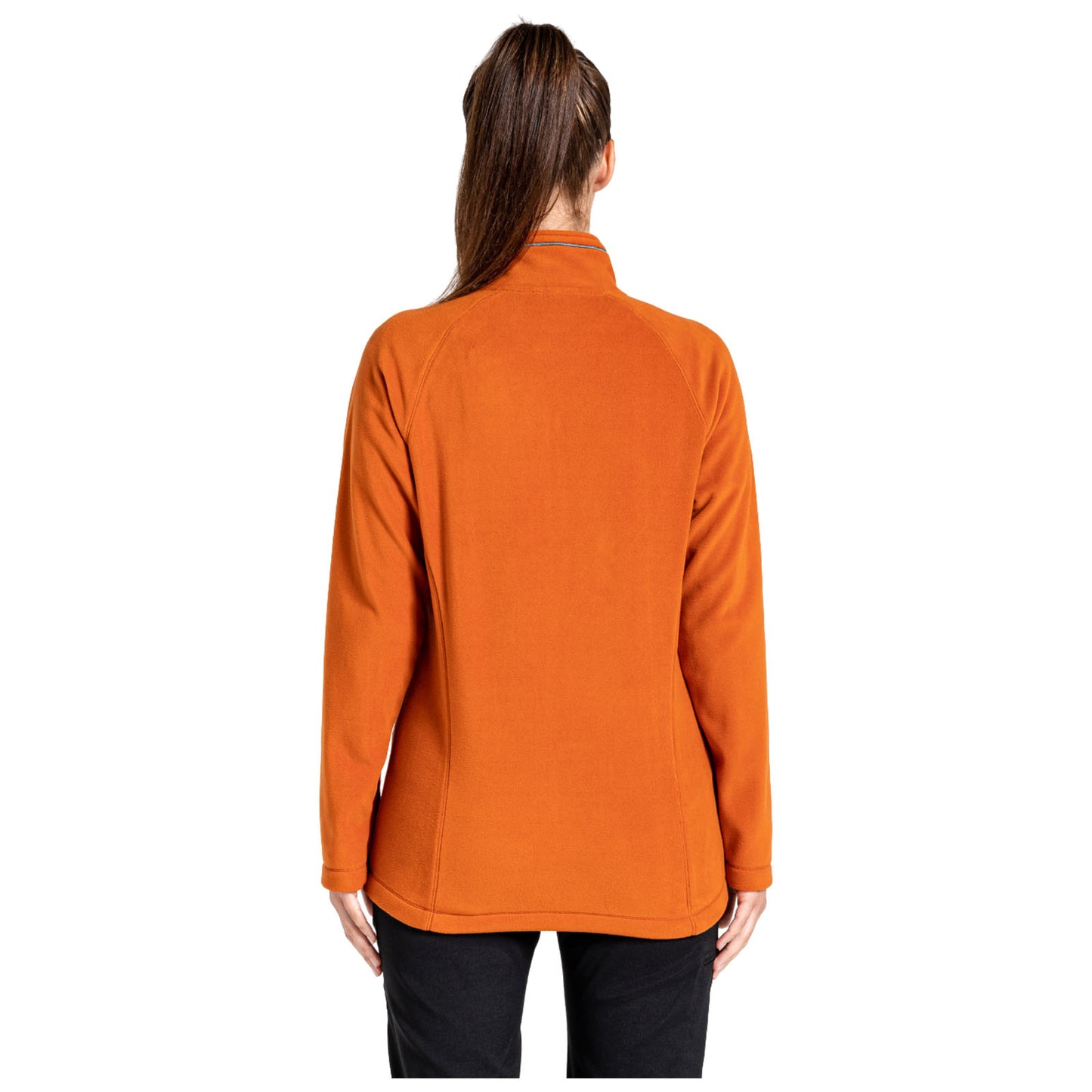 A woman is standing with her back towards the viewer wearing an orange fleece jacket and black pants in a plain white background setting.