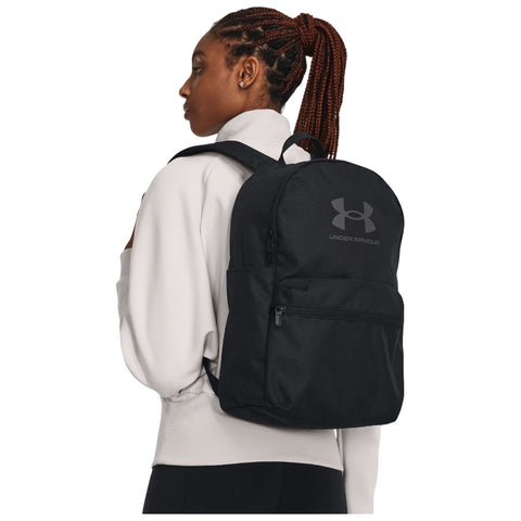 A woman with braided hair wears a black backpack while looking to the side. She is dressed in a light-colored top, standing against a plain background.