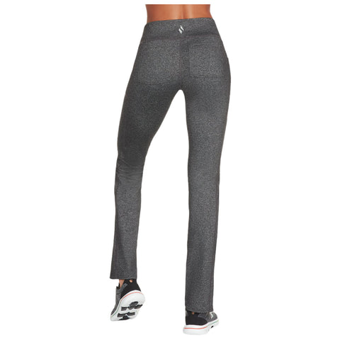 Fitted black leggings with a slight sheen are worn by a person facing away standing in athletic shoes in a neutral background suggesting a casual or active setting.