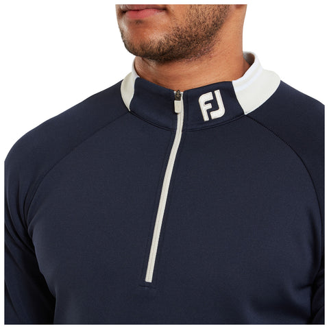 A navy quarter-zip pullover features a white collar and a logo on the left side. The garment is worn by an individual, highlighting the fabric texture and fit.