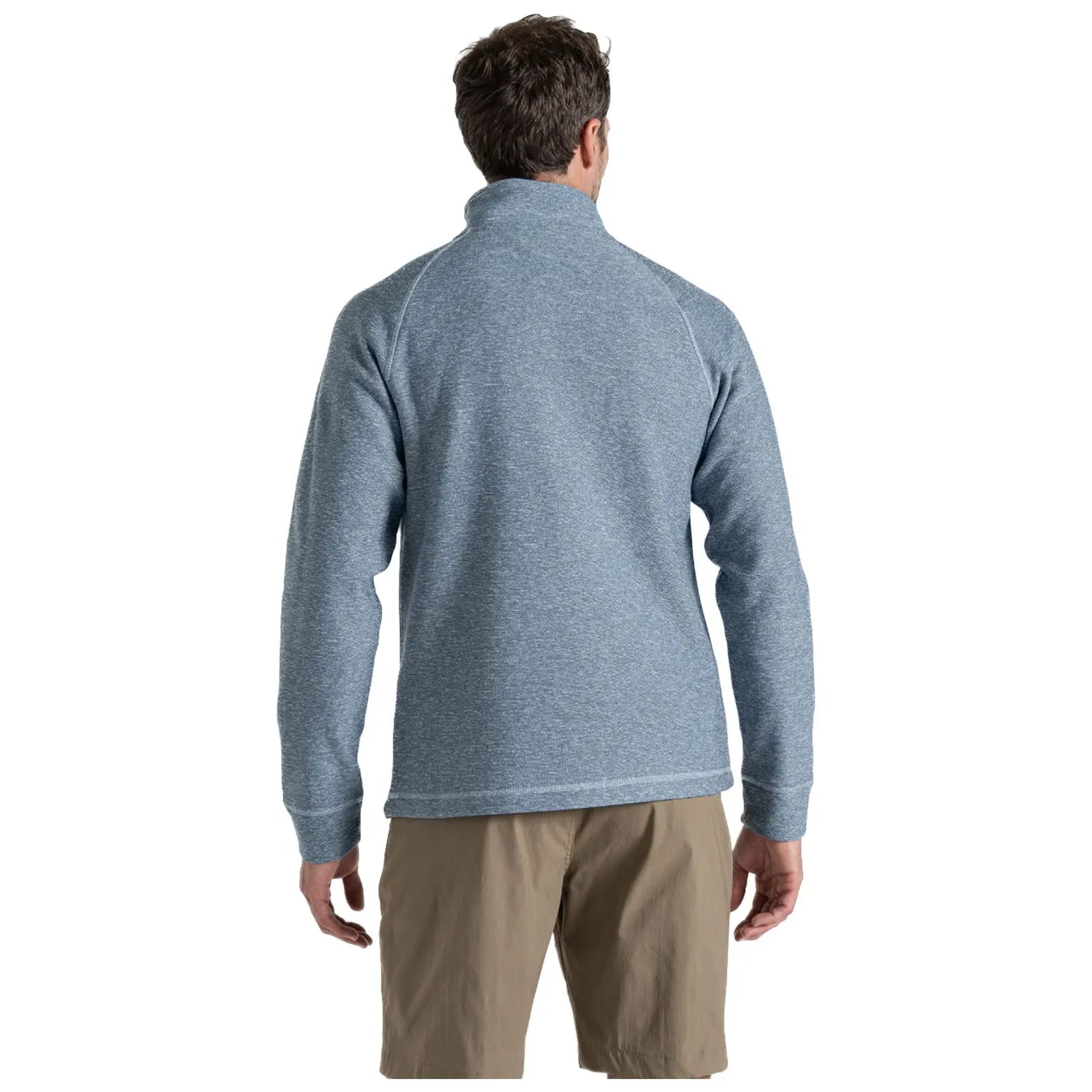 A man stands with his back to the viewer wearing a blue long-sleeve pullover and tan shorts in a neutral setting likely indoors or against a plain background.