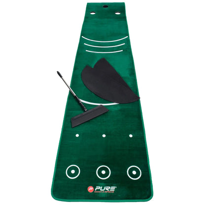 A green putting mat lies flat on a surface featuring guiding stripes and target circles a golf club lies next to the mat along with two black alignment aids and a brush