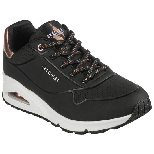A black athletic shoe with a sleek design features a textured upper and bronze accents while resting on a flat surface showcasing its sole and perforated details.