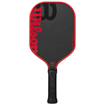 A pickleball paddle with a red outline and a black surface prominently features the word "Wilson" in bold lettering while resting upright against a neutral background.