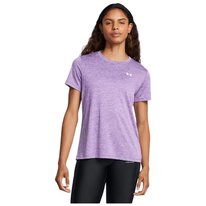 A woman stands confidently wearing a purple athletic t-shirt and black leggings with her arms relaxed at her sides in a neutral background.