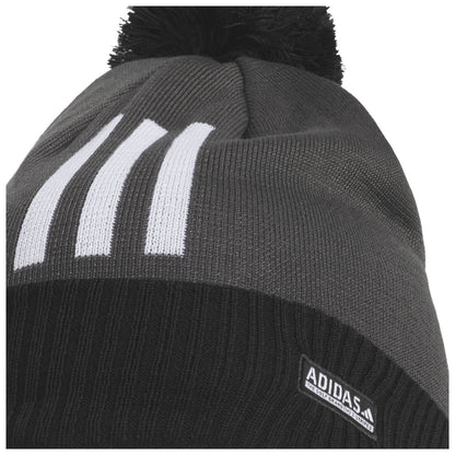 A black and gray knit beanie with a pom-pom on top displays three white stripes on the side and an Adidas logo on the lower edge.