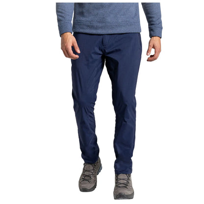 A person stands, wearing navy pants and gray hiking boots, with one hand relaxed by their side, in a neutral background that emphasizes their attire.