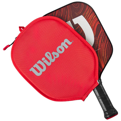 A red carrying case with the Wilson logo contains a paddle with a textured, patterned surface visible through an open zipper, suggesting readiness for play in a sports setting.