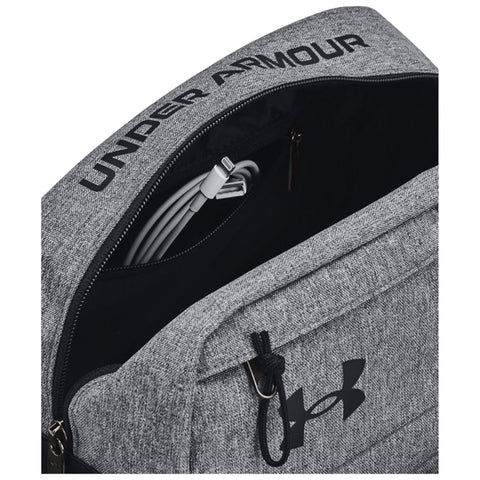 A gray backpack with the text UNDER ARMOUR partially visible on the top is open revealing a charging cable inside against a dark interior background.