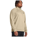 A man is standing confidently wearing a light beige quarter-zip sweatshirt with a black logo on the chest in a neutral background, presenting a casual athletic style.