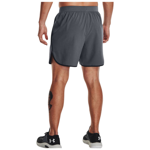 A man is standing with his back facing the viewer wearing gray athletic shorts and black sneakers in a neutral setting. His tattoo is visible on his leg.