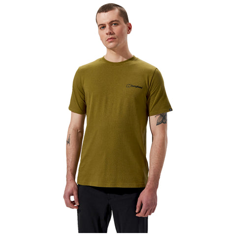 A man stands confidently wearing an olive green short-sleeve t-shirt with a black logo on the left chest area and black pants, set against a plain white background.