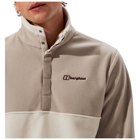 A person is wearing a beige fleece pullover with a half-zip collar and brown logo. The focus is on the upper torso against a white background.