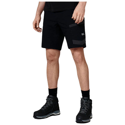 A person is standing wearing black shorts and sturdy black hiking boots with patterned details in a neutral setting without notable background elements.