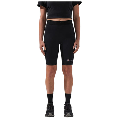 A person stands wearing black bike shorts and a black short-sleeved shirt, paired with black socks and shoes, in a neutral background emphasizing the athletic outfit.