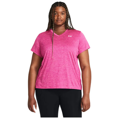 A person stands facing forward wearing a pink athletic t-shirt with short sleeves and a v-neck alongside black pants in a neutral background environment.