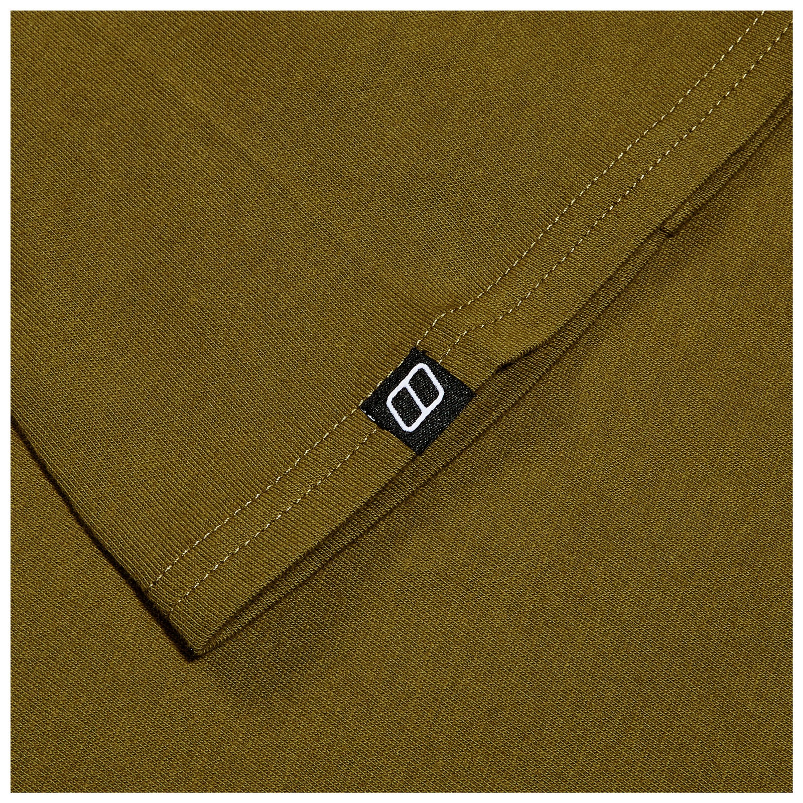 A folded piece of olive green fabric shows a black label with a white logo in the corner while the surrounding texture is smooth and consistent throughout.