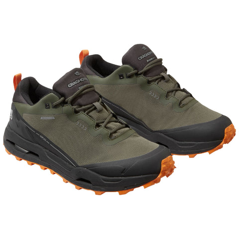 A pair of green and black outdoor shoes is displayed with rubber soles featuring orange traction lugs showing their design for hiking or trail walking in rugged environments.