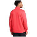 A man stands with his back to the viewer wearing a bright coral jacket with a high collar in a neutral background, emphasizing the jacket's color and style.