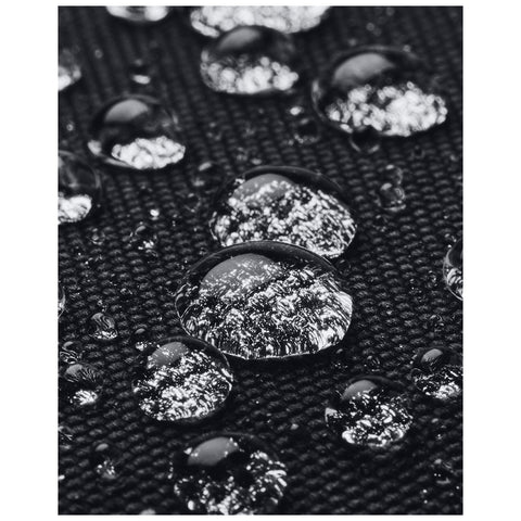 Water droplets rest on a textured black surface reflecting light while appearing clear and glossy in a close-up view showcasing the contrast between the droplets and the background.